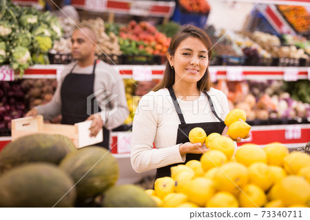 Merchandiser lays out ripe lemons on the shelves in supermarket Merchandiser lays out ripe lemons on the shelves in supermarket 73340711