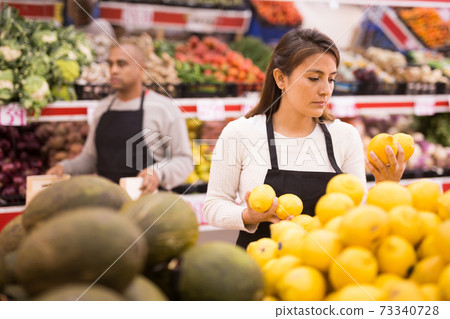 Merchandiser lays out ripe lemons on the shelves in supermarket Merchandiser lays out ripe lemons on the shelves in supermarket 73340728