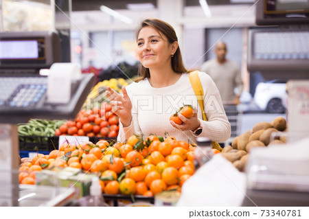 Female shopper selects ripe tangerines in grocery hypermarket Female shopper selects ripe tangerines in grocery hypermarket 73340781