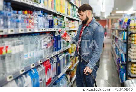 Portrait of focused young man purchasing bottled water in grocery store Portrait of focused young man purchasing bottled water in grocery store 73340940