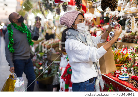 Woman in protective mask chooses christmas balls at christmas fair Woman in protective mask chooses christmas balls at christmas fair 73340941