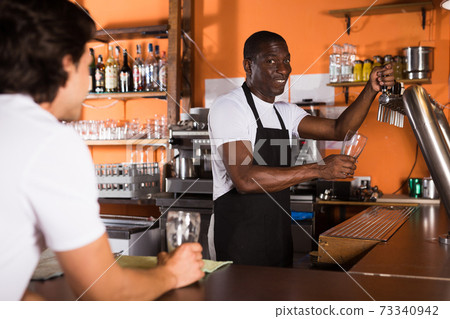Young man barman is pouring unbottled beer for client 73340942