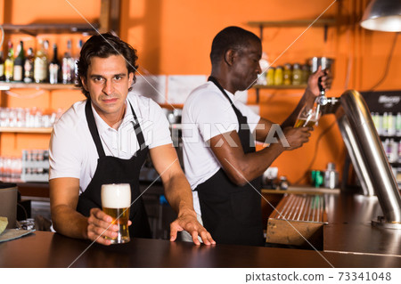 Bartender offering glass of beer, man pouring beer on background Bartender offering glass of beer, man pouring beer on background 73341048