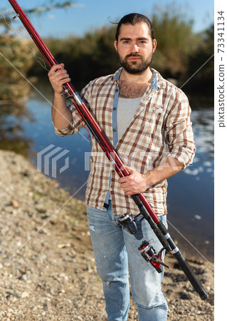 Adult man standing outdoors with angling rod planning to fishing Adult man standing outdoors with angling rod planning to fishing 73341134