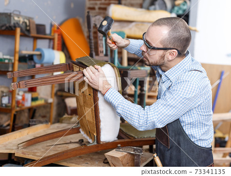 Craftsman reupholstering chair in workshop Craftsman reupholstering chair in workshop 73341135