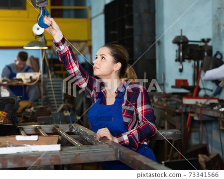 Girl worker is holding lift hook equipment in workshop. Girl worker is holding lift hook equipment in workshop. 73341566