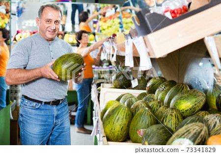Smiling male is choosing green melon in the supermarket. 73341829