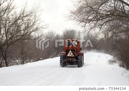 Old tractor clears the snow-covered road from snow blockages Old tractor clears the snow-covered road from snow blockages 73344134