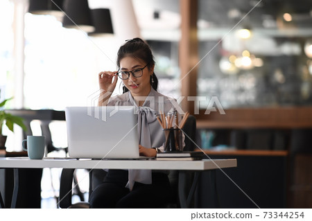 Businesswoman hand touching her spectacles and working on laptop at office. Businesswoman hand touching her spectacles and working on laptop at office. 73344254