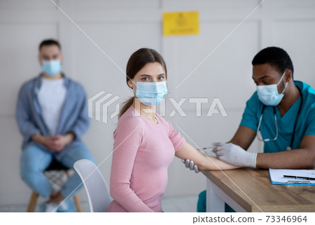 Black male doctor giving intramuscular injection to young woman at medical office Black male doctor giving intramuscular injection to young woman at medical office 73346964