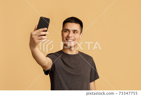 Modern photo on gadget for blog. Cheerful millennial male student makes selfie 73347755