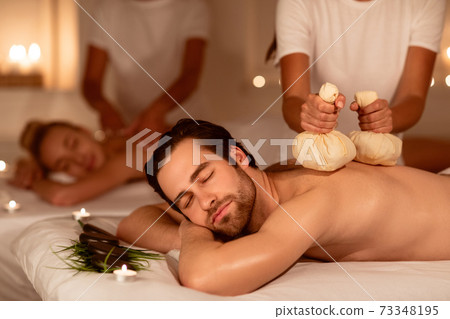 Couple Relaxing During Herbal Back Massage With Aromatic Bags Indoors Couple Relaxing During Herbal Back Massage With Aromatic Bags Indoors 73348195
