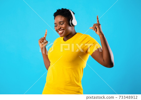 Joyful Plus-Size African Woman Dancing Listening To Music, Blue Background Joyful Plus-Size African Woman Dancing Listening To Music, Blue Background 73348912