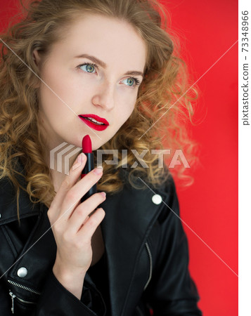 Portrait of young girl painting her lips with matte red lipstick on red background. Beauty, fashion concept. Portrait of young girl painting her lips with matte red lipstick on red background. Beauty, fashion concept. 73348966