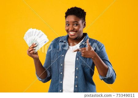 Plus-Size Black Woman Holding Cash Of Euro Money, Yellow Background 73349011