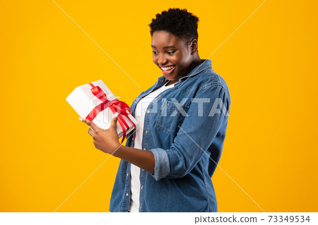 Happy Oversized Black Woman Holding Gift Standing Over Yellow Background 73349534