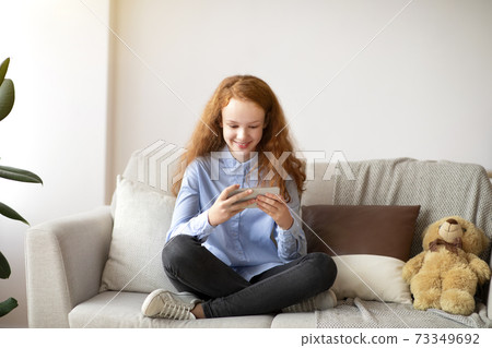 Girl using her smart phone resting on sofa Girl using her smart phone resting on sofa 73349692