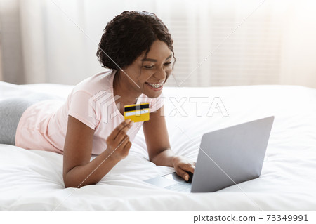 Happy woman shopping with credit card and laptop in bed Happy woman shopping with credit card and laptop in bed 73349991