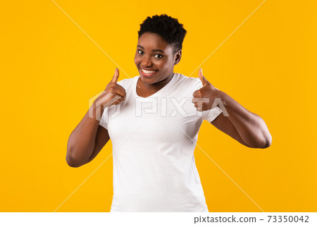 Cheerful Overweight African Woman Gesturing Thumbs-Up Standing On Yellow Background 73350042
