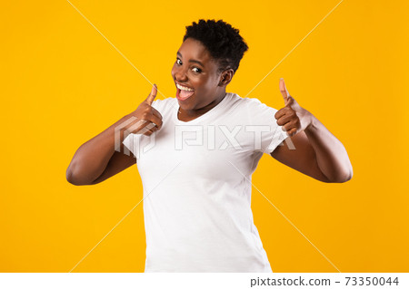 Plus-Size Black Lady Gesturing Thumbs-Up With Both Hands, Yellow Background Plus-Size Black Lady Gesturing Thumbs-Up With Both Hands, Yellow Background 73350044
