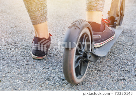 Legs of a man riding a scooter on the street. 73350143