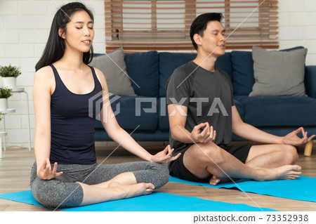 Healthy young Asian couple attractive couple practicing yoga exercises sitting on a mat in lotus pose in an online class on quarantine at home. Concept of Technology for New normal lifestyle Healthy young Asian couple attractive couple practicing yoga exercises sitting on a mat in lotus pose in an online class on quarantine at home. Concept of Technology for New normal lifestyle 73352938