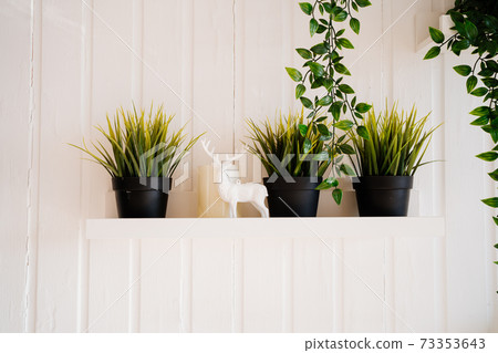 artificial flowers in pots on shelves against the white wall. 73353643