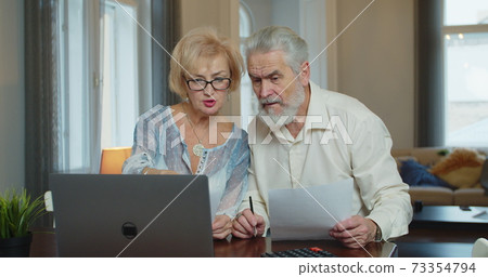 Senior man and woman paying bills and managing budget. Mature worried couple sitting and managing expenses at home. Senior man and woman paying bills and managing budget. Mature worried couple sitting and managing expenses at home. 73354794