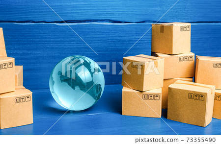Planet Earth globe and cardboard boxes mass consumption products. Delivering goods around the world. International trade and transportation of goods. Shipping freight. Transnational business industry. Planet Earth globe and cardboard boxes mass consumption products. Delivering goods around the world. International trade and transportation of goods. Shipping freight. Transnational business industry. 73355490