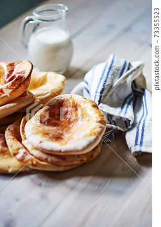 Close up of flatbread pita with milk at the wodden white table. Fried ohnny cake. Eastern cuisine. Asia flapjack. Rustic stile. Close up of flatbread pita with milk at the wodden white table. Fried ohnny cake. Eastern cuisine. Asia flapjack. Rustic stile. 73355523