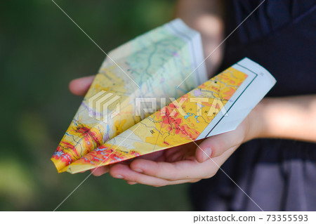 a paper airplane made from a geographical map. girl child holding a plane made of paper in her hand close-up. 73355593