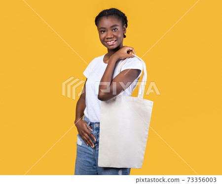 African American Woman Holding White Eco Bag Over Yellow Background African American Woman Holding White Eco Bag Over Yellow Background 73356003