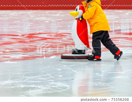 A teenager learns to skate on an ice rink holding on to an assistant, a toy penguin. A teenager learns to skate on an ice rink holding on to an assistant, a toy penguin. 73356208