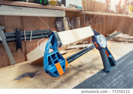 Joining wooden handmade box with clamps joiners after glueing. Different chisels, drills and pencils at craftsman workshop. DIY instruments on wood workbench. Workplace organization arrangement 73356232