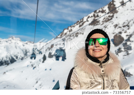 Young adult beautiful happy attractive caucasian smiling woman enjoy ascent sitting inside ski lift gondola cable car against skiing resort panorama breathtaking view. Winter travel welcome concept 73356757