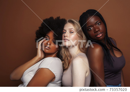 young pretty caucasian, afro, scandinavian woman posing cheerful together on brown background, lifestyle diverse nationality people concept 73357020