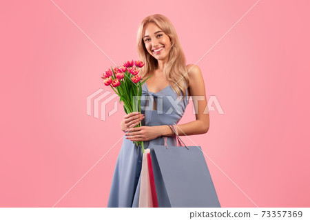Portrait of pretty young lady with bouquet of tulips and gift bags shopping for spring holiday, pink studio background Portrait of pretty young lady with bouquet of tulips and gift bags shopping for spring holiday, pink studio background 73357369