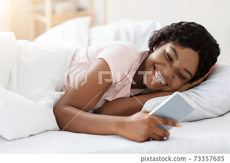 Happy young black woman using smartphone in bed Happy young black woman using smartphone in bed 73357685