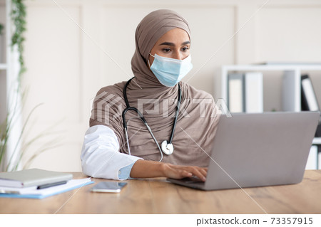 Young female doctor in face mask using laptop Young female doctor in face mask using laptop 73357915