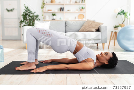 Side view of athletic black lady doing abs exercise, standing in yoga pose during her home workout Side view of athletic black lady doing abs exercise, standing in yoga pose during her home workout 73357937