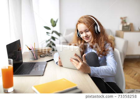 Girl wearing headphones enjoying podcast using tablet 73358258