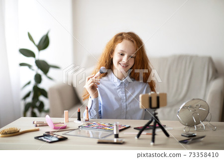 Teen showing face powder, recording beauty blog on phone 73358410