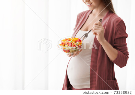 Pregnant Woman With Bowl Of Vegetable Salad Standing Near Window At Home Pregnant Woman With Bowl Of Vegetable Salad Standing Near Window At Home 73358982
