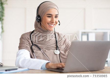 Cheerful muslim lady doctor having video chat with patient Cheerful muslim lady doctor having video chat with patient 73358985