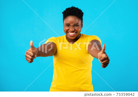 Plus-Size Black Woman Gesturing Thumbs-Up With Both Hands, Blue Background Plus-Size Black Woman Gesturing Thumbs-Up With Both Hands, Blue Background 73359042