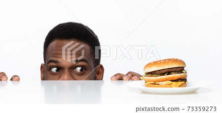 Hungry African Guy Looking At Burger On Desk In Studio 73359273