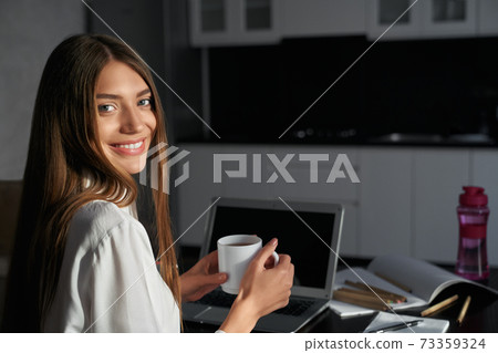 Smiling woman drinking tea while relaxing during education 73359324