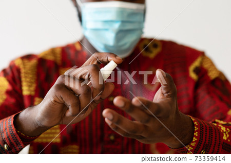 Unrecognizable African Man In Protective Mask Applying Sanitizer Antibacterial Spray On Hands 73359414