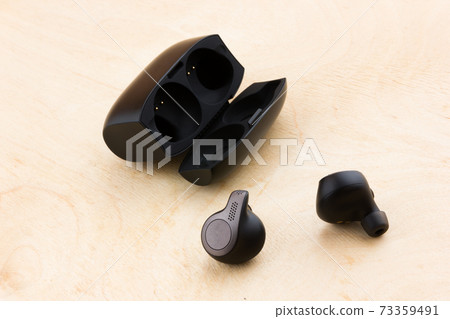 Wireless headphones on a wooden surface. Wireless headset and charging case on a wooden table. 73359491