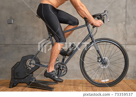 Athletic young man riding stationery bike at home Athletic young man riding stationery bike at home 73359537